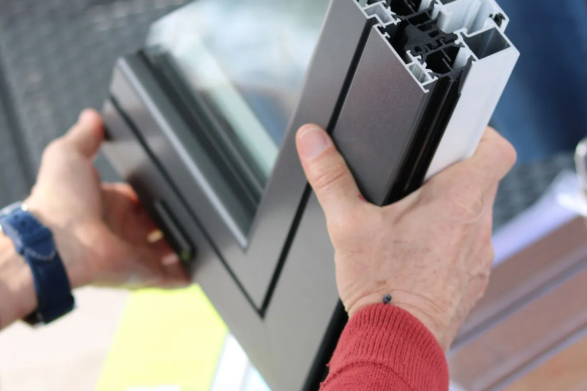 Hands holding a cut section of a modern aluminum window frame