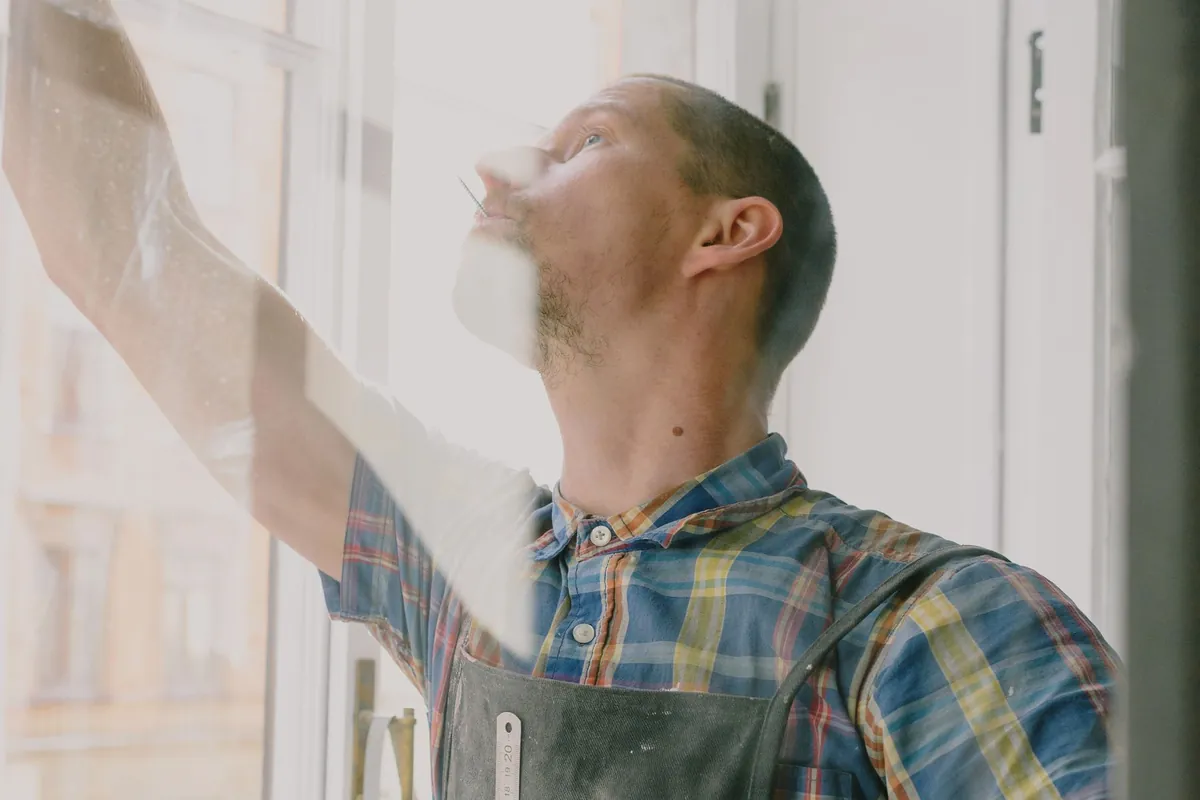 Installer in a work apron setting a tall white window frame